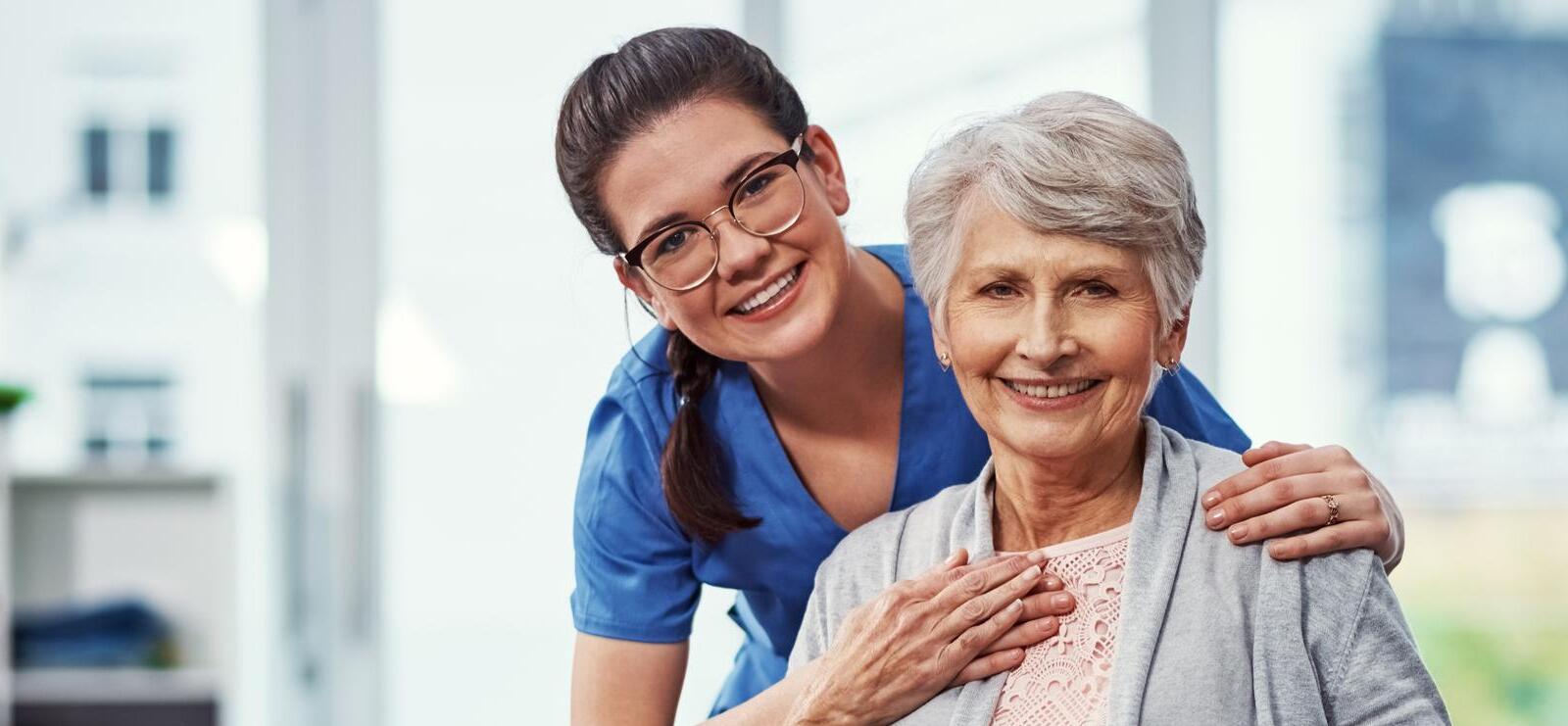 Cuidadora sorridente apoiando a mão no ombro de uma senhora idosa
