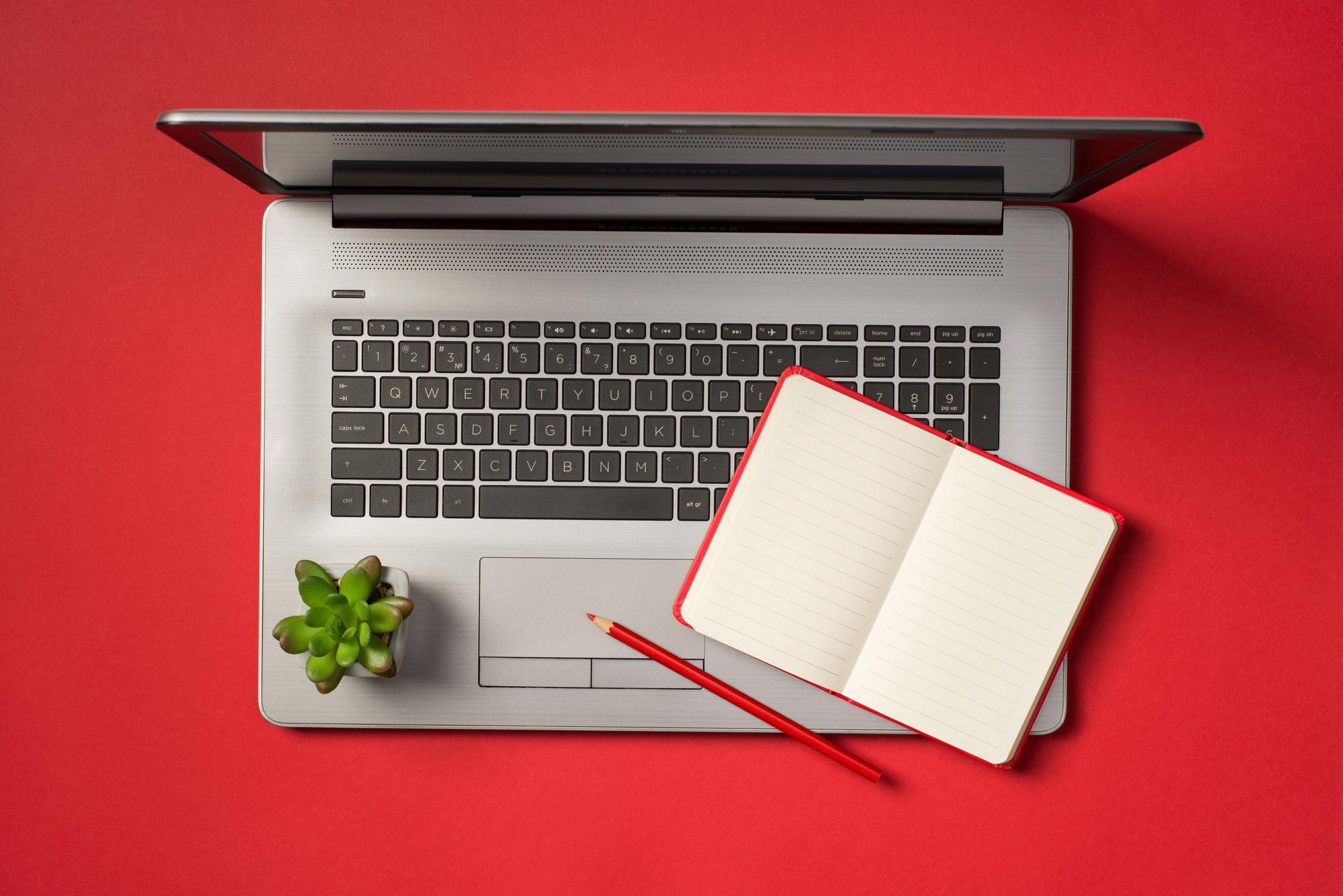 Laptop em fundo vermelho com lápis e caderno ao lado